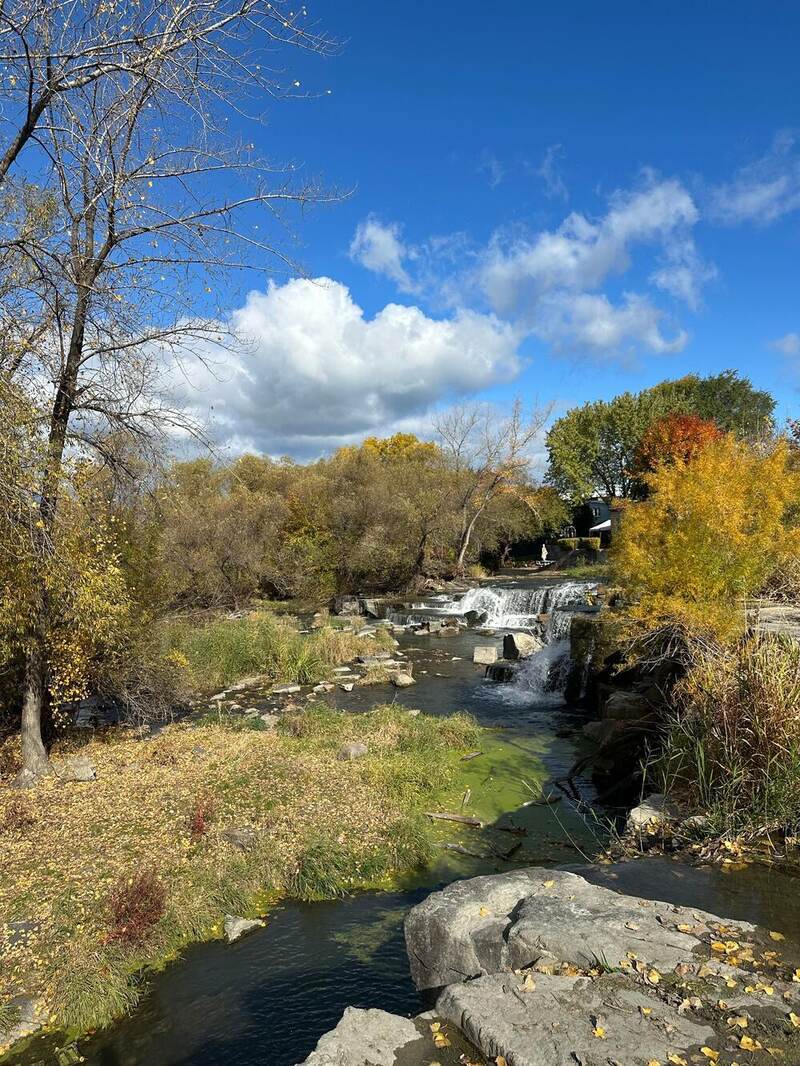 A small waterfall and creek under a blue sky with puffy clouds